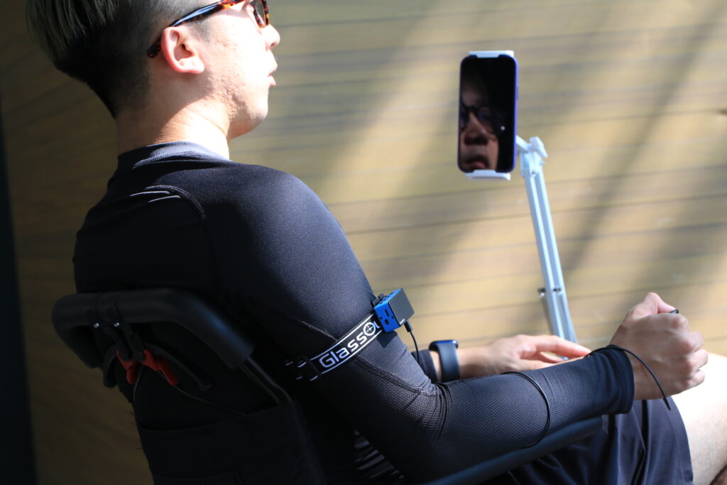 a man in a wheel chair with his phone mounted in front of him. He has a glassouse link on his arm and is using a switch which is attached to the link.